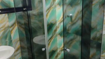 Un baño con cabina de ducha de vidrio, un lavabo blanco y una pared con diseño de mármol.