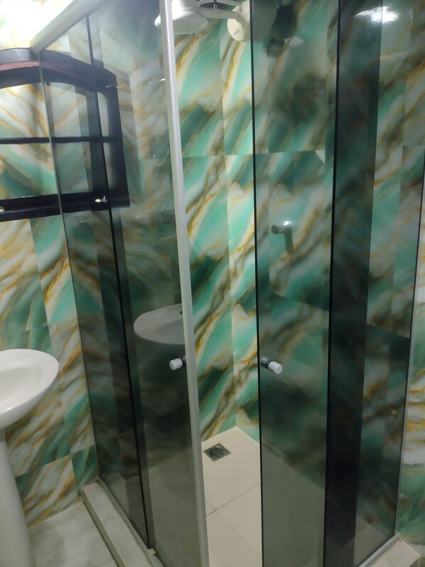 Un baño con cabina de ducha de vidrio, un lavabo blanco y una pared con diseño de mármol.