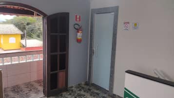 Corredor com extintor, porta e vista para um edifício amarelo lá fora.