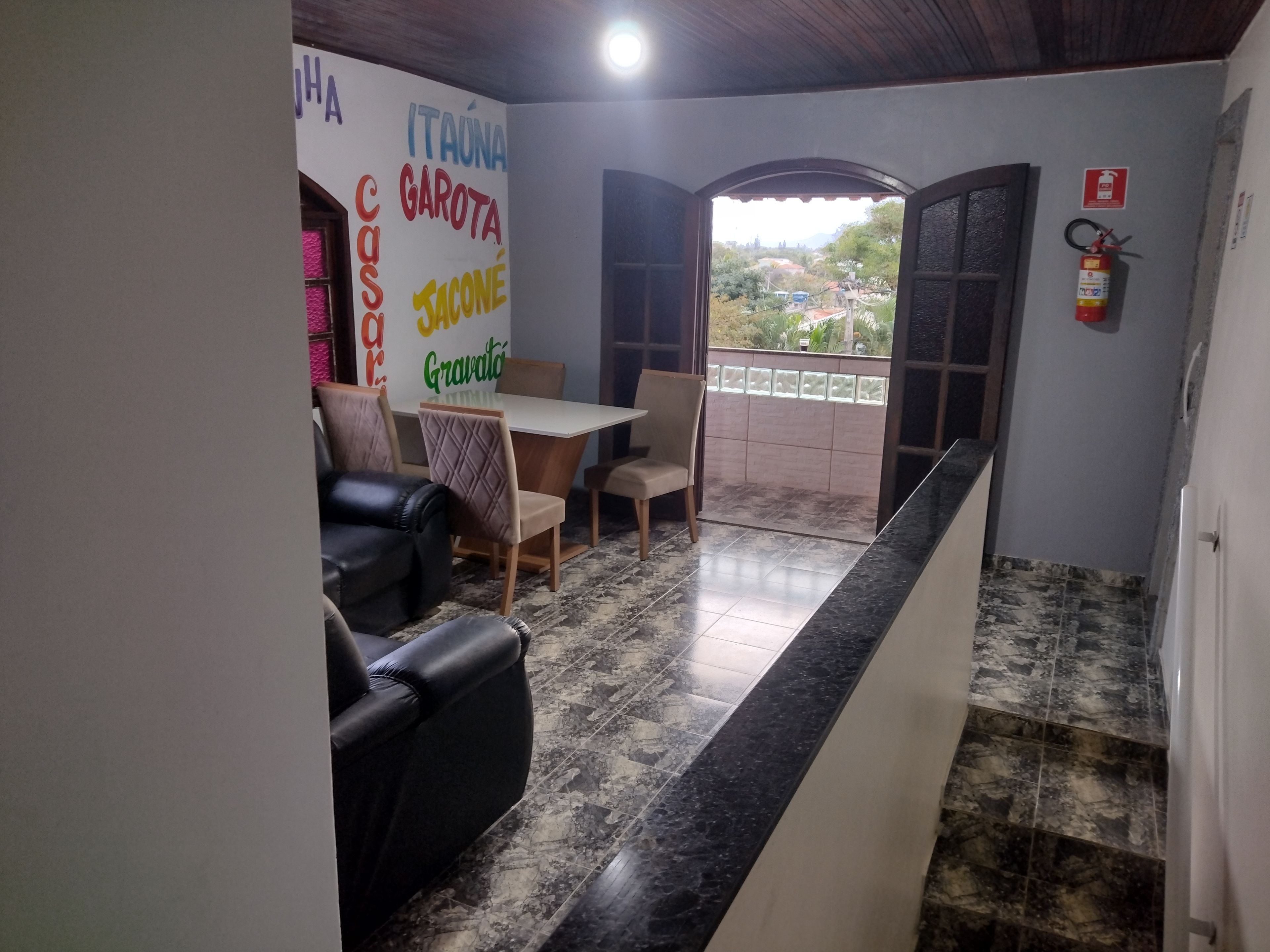 A dining area with a table and chairs, a black leather sofa, and a view through an open door to a balcony.