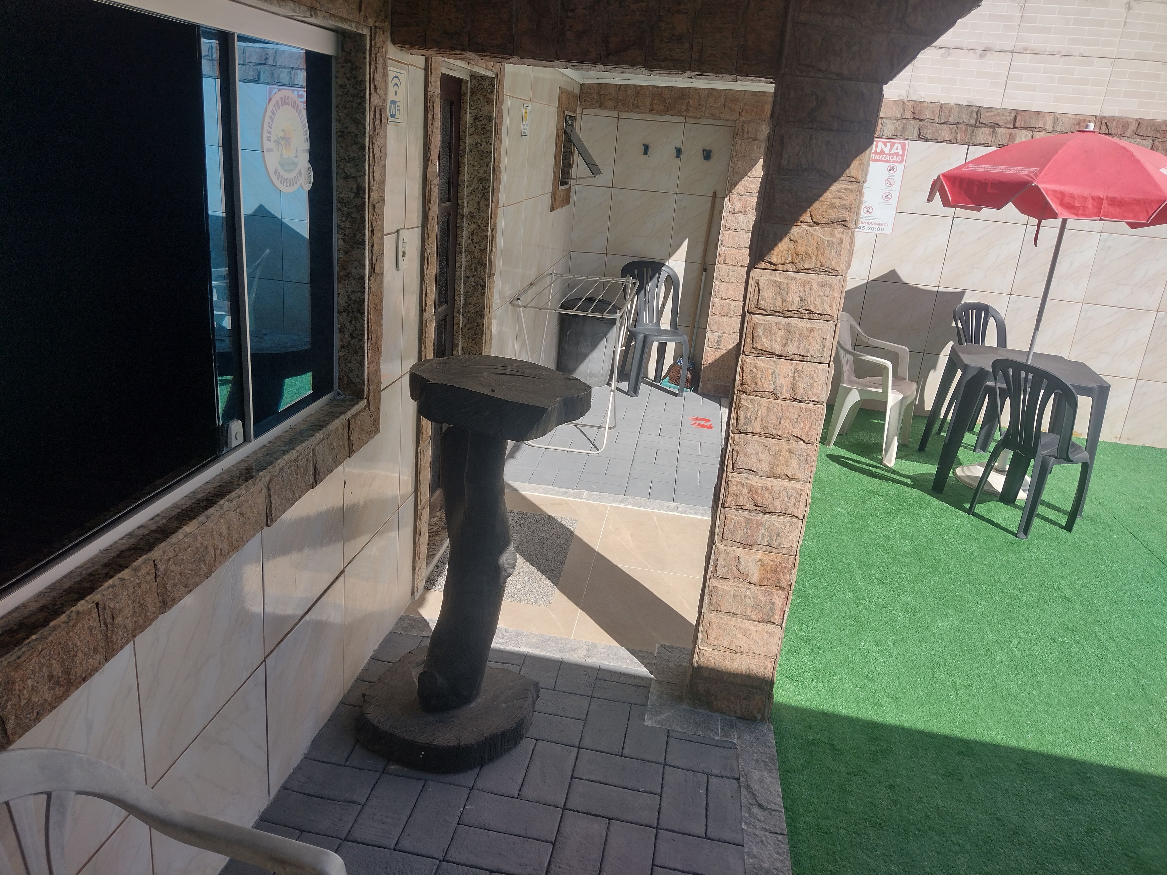 A patio area with a table and chairs, a red umbrella, and a view of the interior through a glass door.