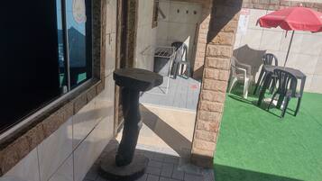 A patio area with a table and chairs, a red umbrella, and a view of the interior through a glass door.