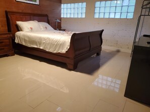 A bedroom with a wooden bed, a nightstand, a lamp, and a window with blinds. - Remodeled Artist Studio in Coconut Grove (Miami)