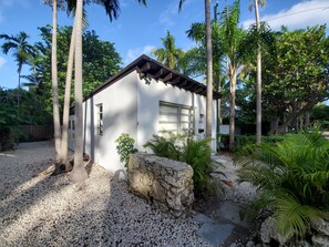 A small white building with a garage, surrounded by palm trees and gravel.