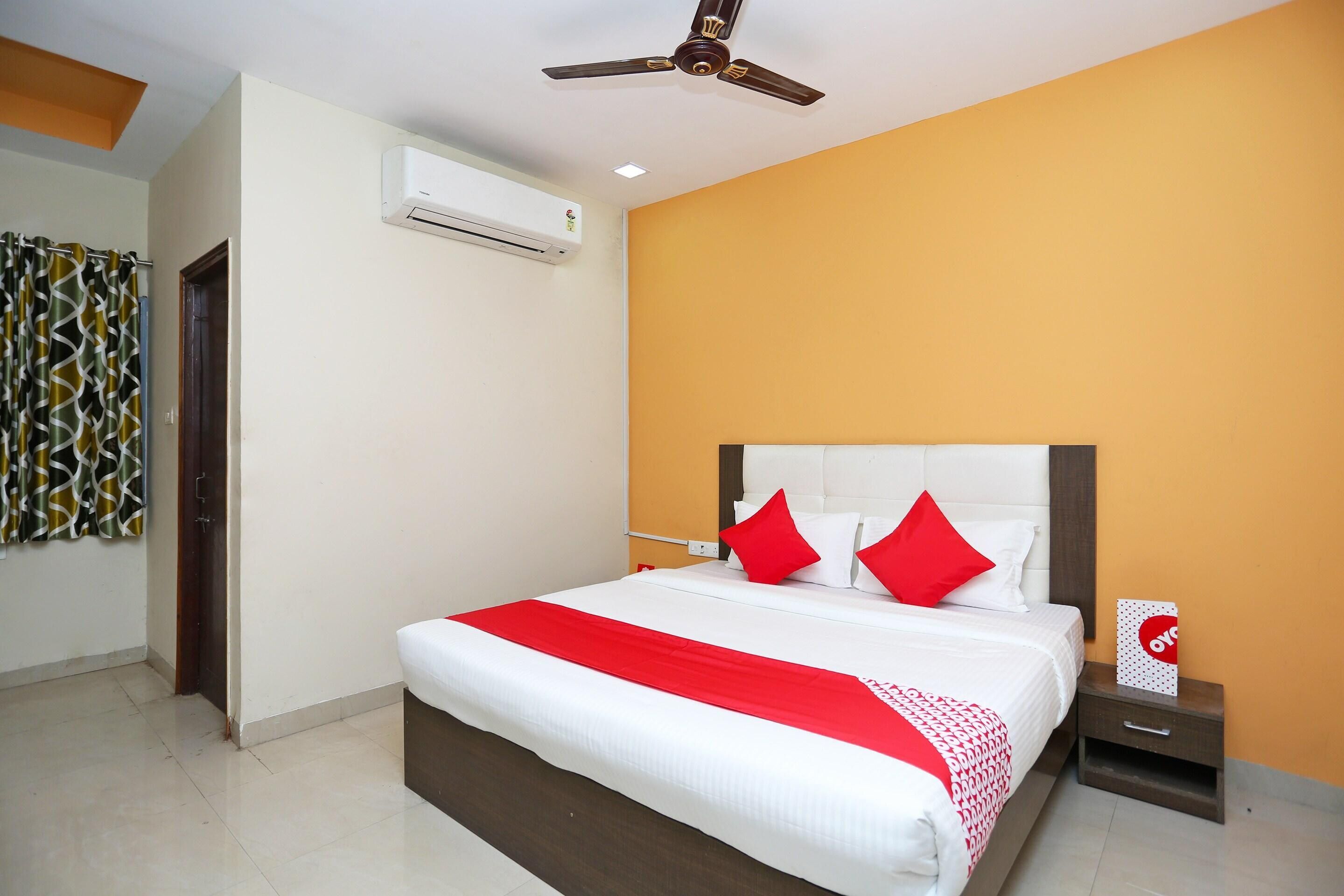 A hotel room with a bed, a nightstand, a wall-mounted air conditioner, and a ceiling fan.
