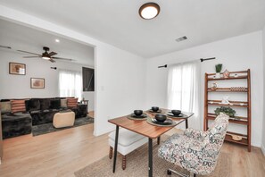 Ein modernes Wohnzimmer mit einer Couch, einem Esstisch gedeckt mit Schalen, einem Deckenventilator und einem Holzregal mit Dekorationselementen.