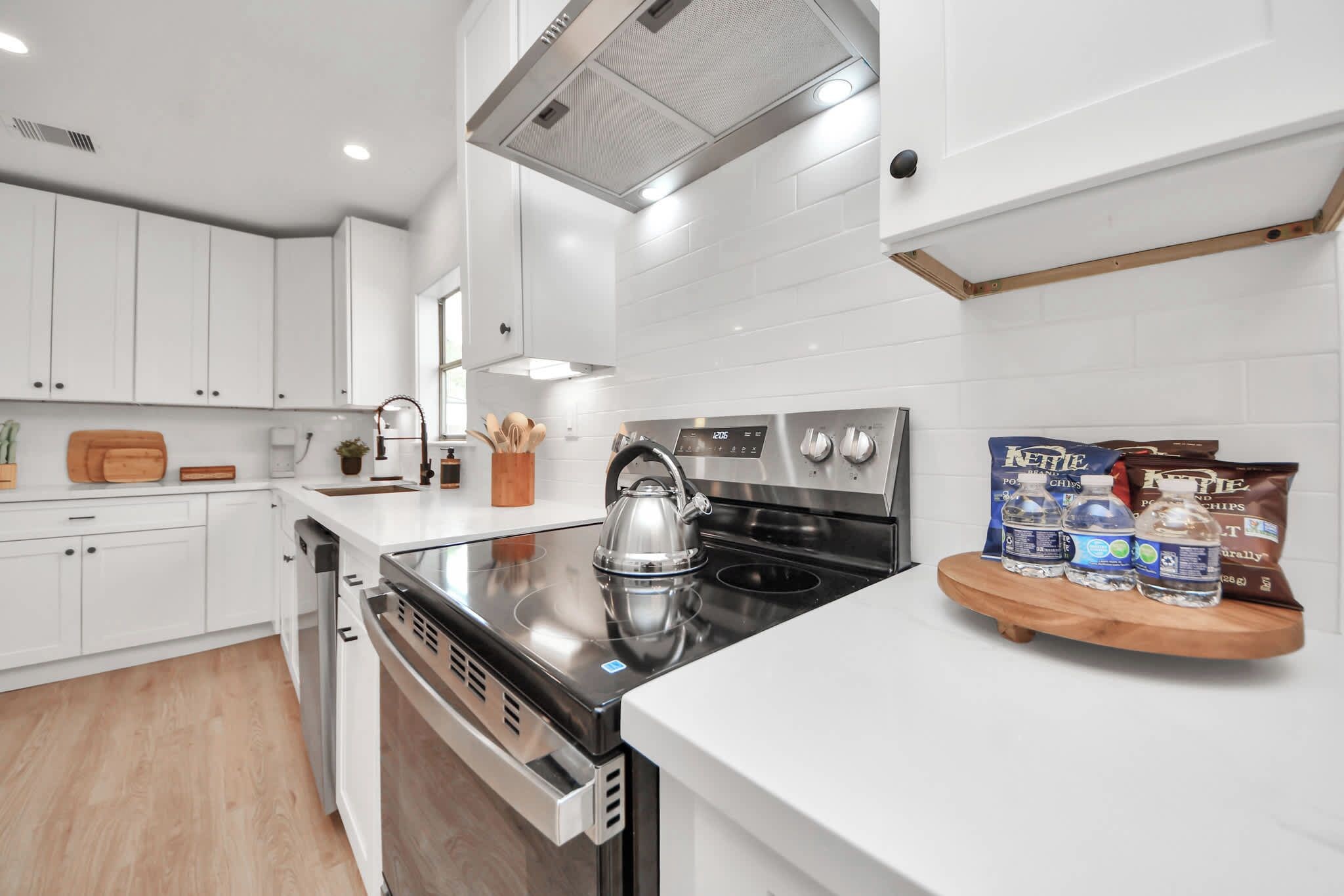 A modern kitchen with white cabinetry, a stainless steel stove, and a kettle on the counter.