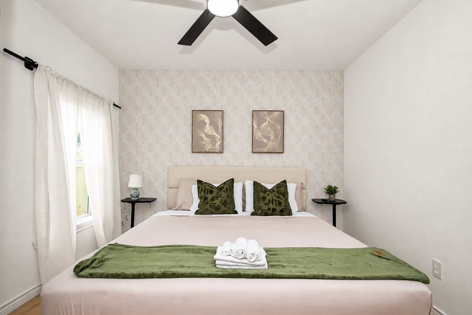 A hotel bedroom with a bed, two nightstands, a ceiling fan, and artwork on the wall.