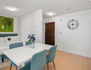 A modern room with a white dining table, teal chairs, a green accent wall, and a wall clock. - Cozy Place Steps to CN Tower & Rogers Center (Toronto)