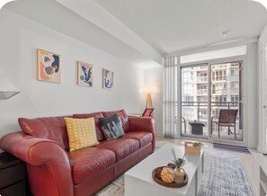 A modern living room with a red leather sofa, a white coffee table, and artwork on the walls. - Cozy Place Steps to CN Tower & Rogers Center (Toronto)