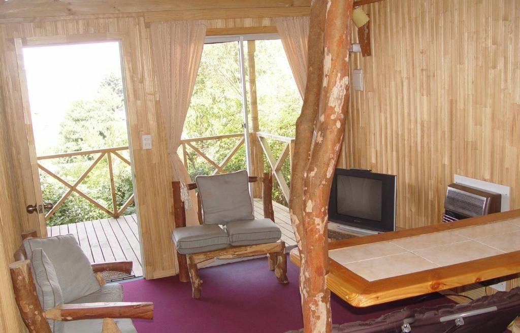A wooden cabin with a balcony, a television, and a table.
