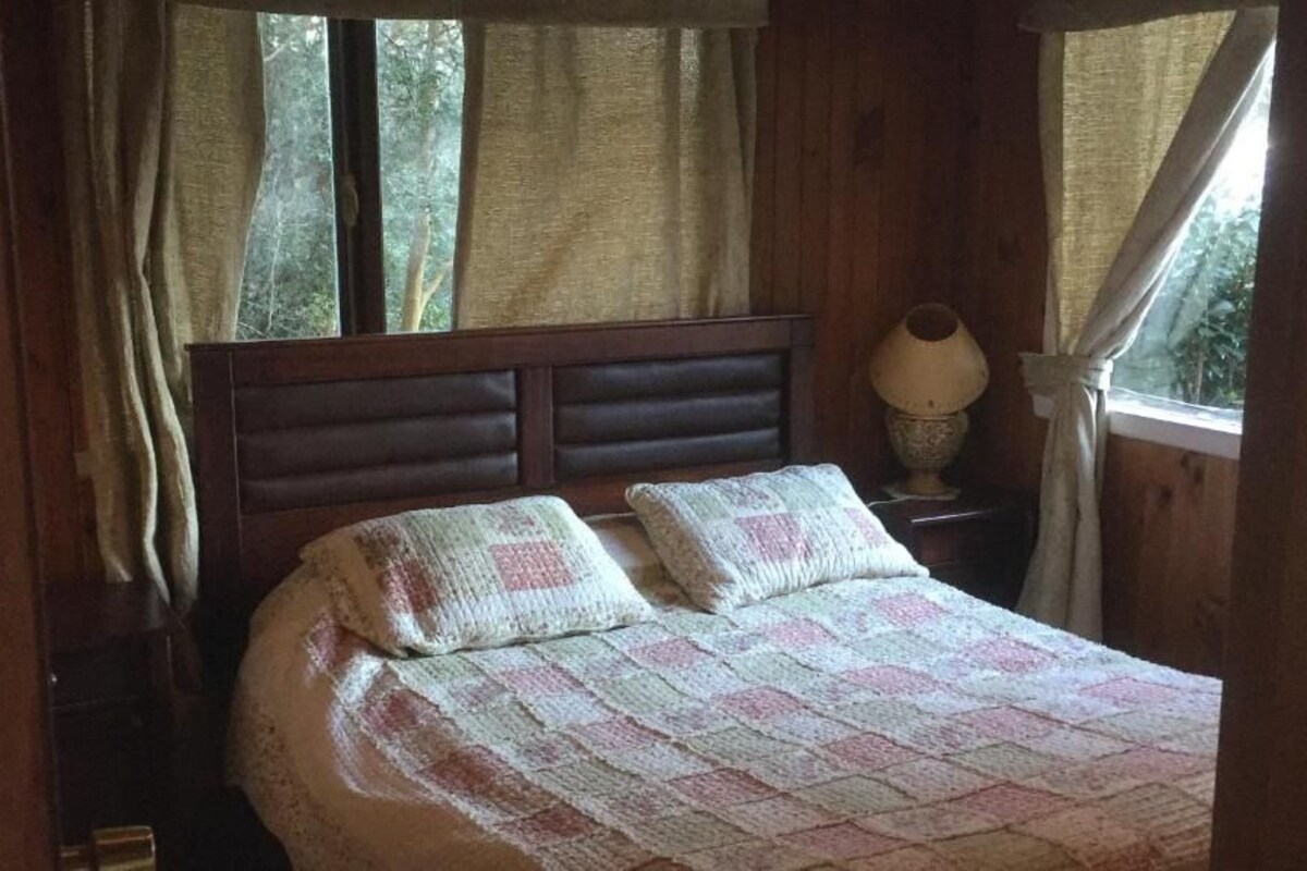 Un lit avec une couette, une table de chevet avec une lampe et des rideaux à une fenêtre.