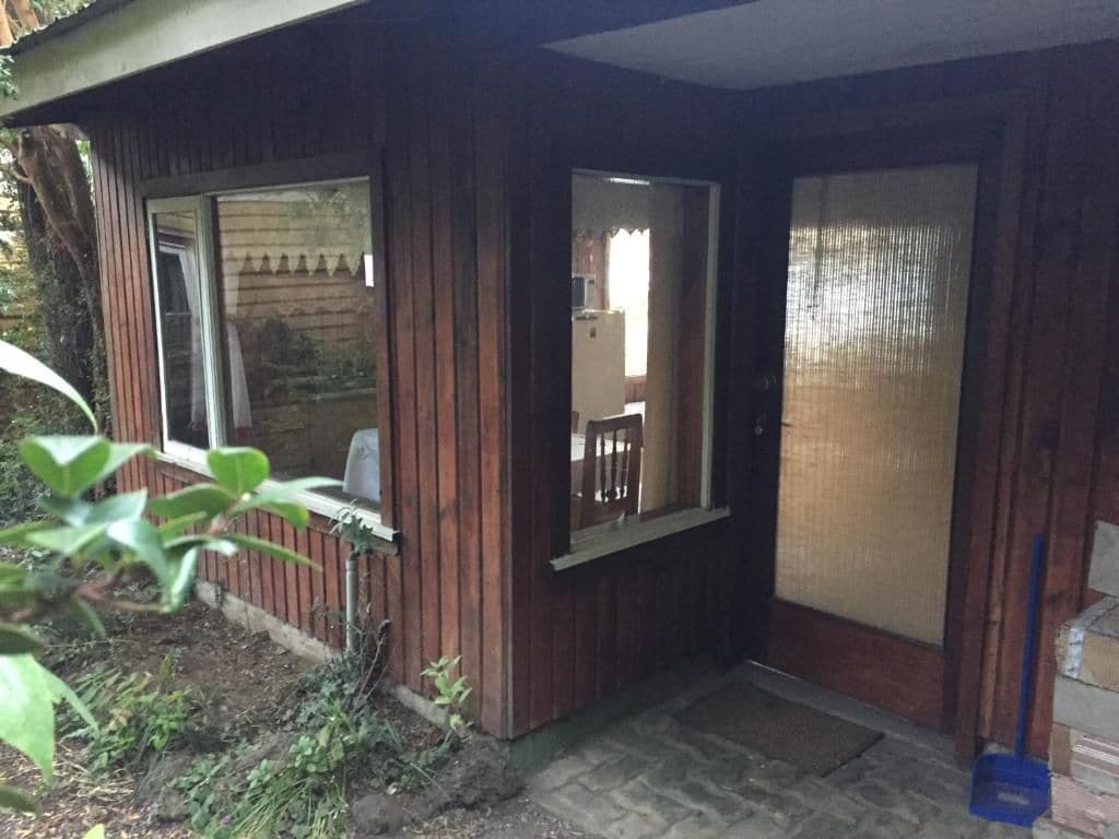 Una cabaña de madera con ventana, puerta y un pequeño porche.