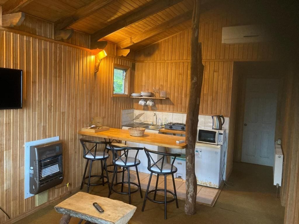 Une cuisine compacte avec un intérieur en bois, un coin bar avec des tabourets, un téléviseur fixé au mur et un four à micro-ondes.