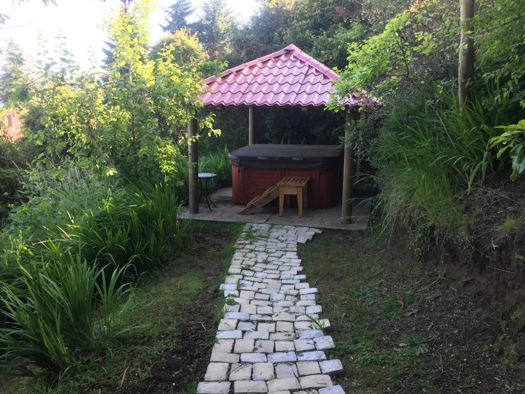 Un jardin avec un chemin en briques menant à une structure en bois surmontée d’un toit rouge.