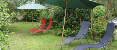 Un jardin avec deux chaises longues sous un parasol vert, entouré de verdure.