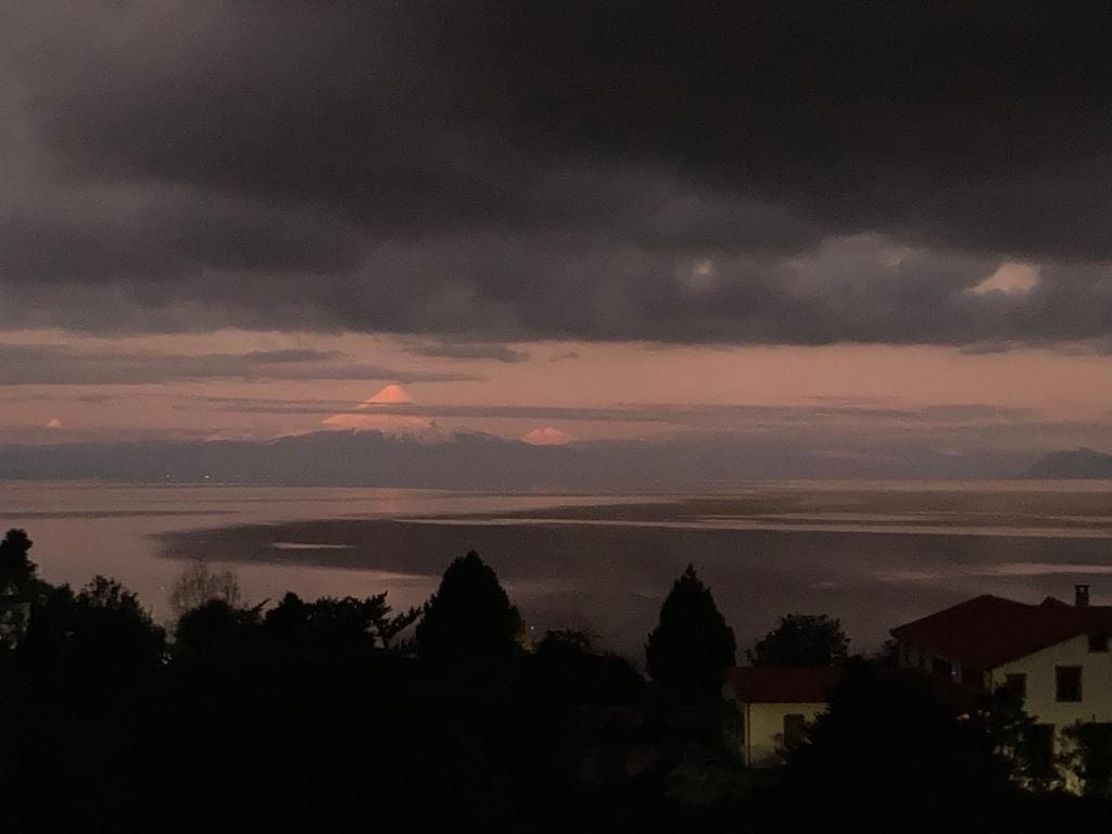 Vista de un lago con una montaña al fondo, rodeado de árboles y un edificio con techo rojo.