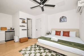 Ein Schlafzimmer mit einem Bett, einem Nachttisch, einem Deckenventilator, einer Wand-Klimaanlage und einer Tür zu einem anderen Raum.