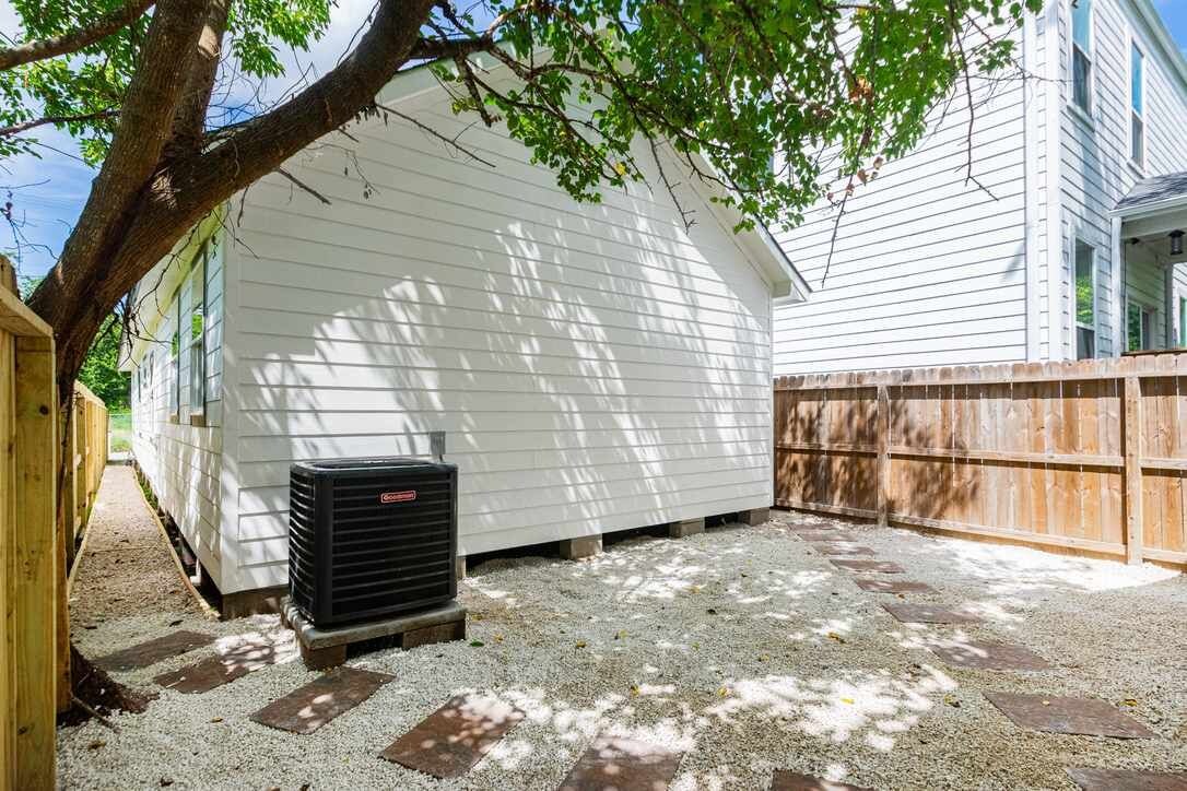 A covered outdoor area with a white building, a wooden fence, and a gravel ground.