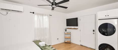 A bedroom with a bed, a ceiling fan, a TV, a washing machine, and a door.