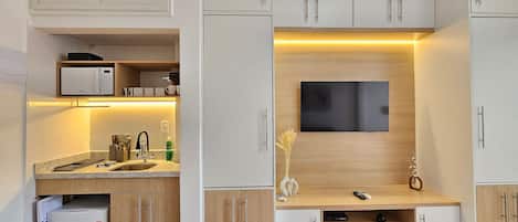 A modern kitchen with a built-in microwave, coffee maker, and a flat-screen TV mounted on the wall.