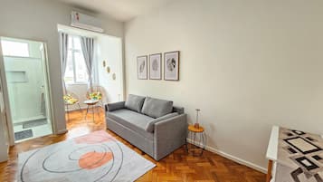 Sala de estar com um sofá cinza, uma mesa redonda pequena e um tapete estampado.