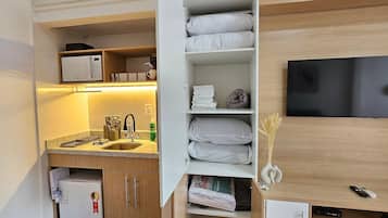A compact hotel room with a kitchenette, a flat-screen TV mounted on the wall, and a small refrigerator.