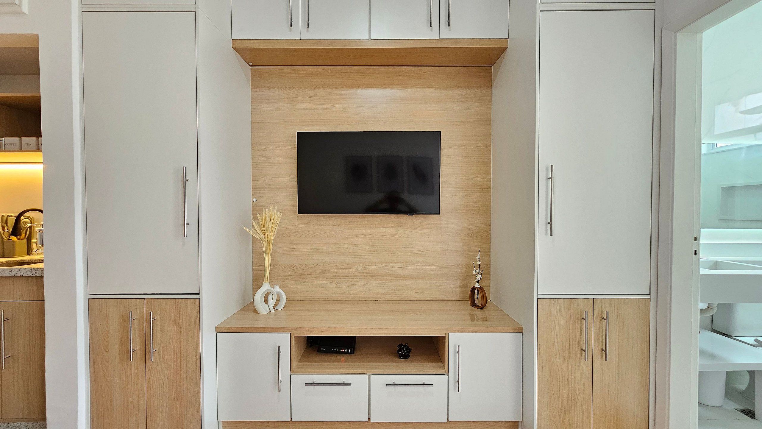 A modern kitchen with a built-in TV, wooden cabinets, and a coffee machine.