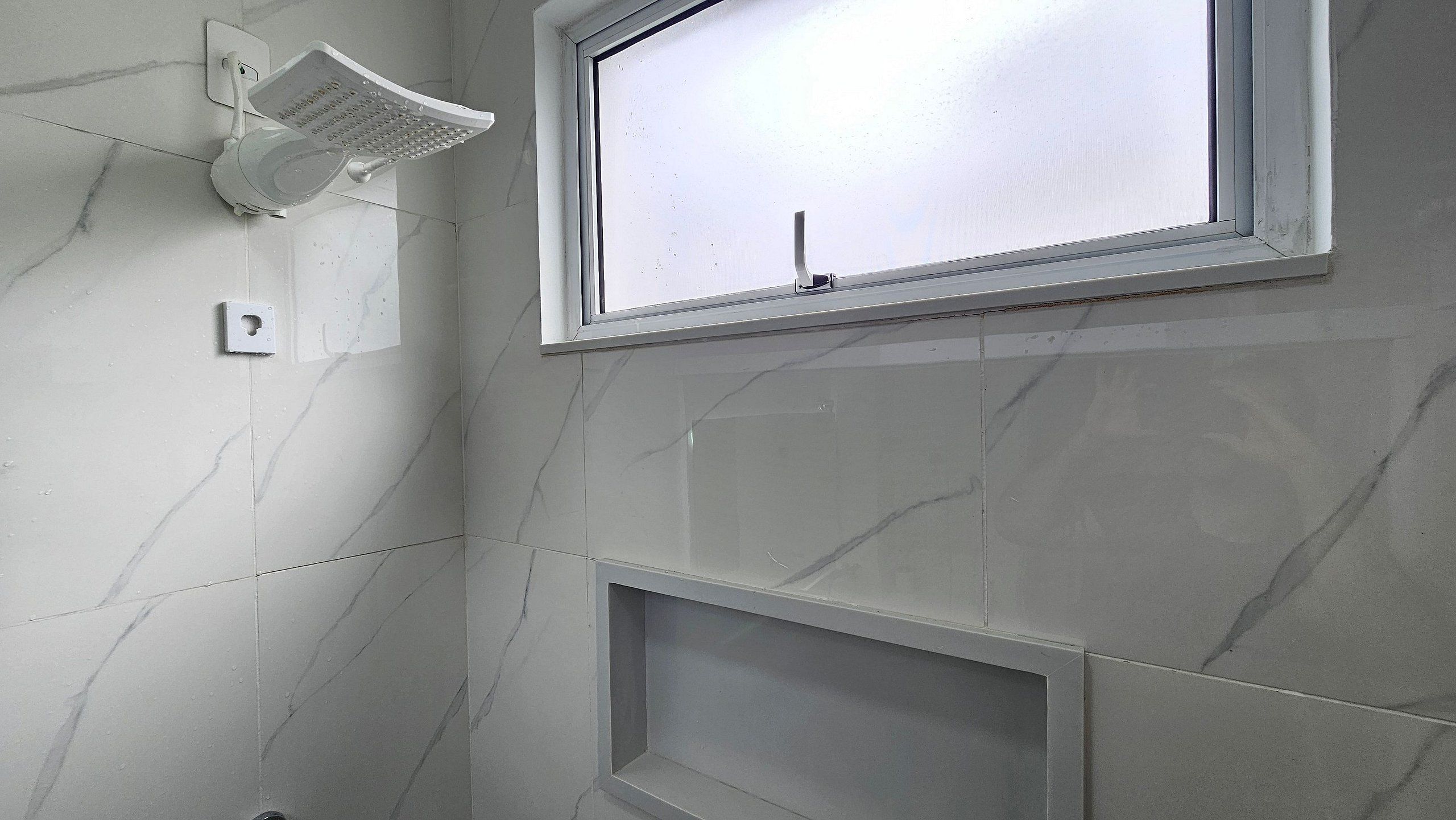 A bathroom with a shower, a window, and a tiled wall.