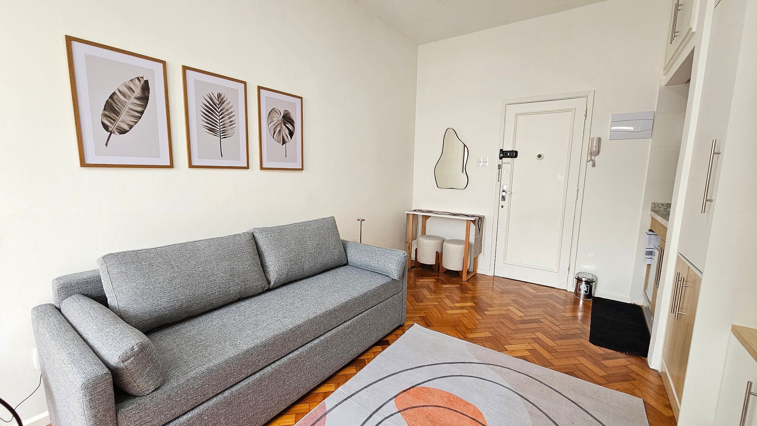 Un salon avec un canapé gris, une petite table et une porte dotée d’un miroir.