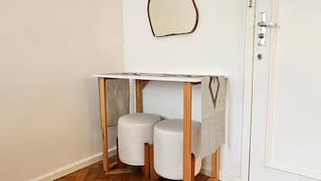 Uma mesa pequena de madeira branca com tampo estampado, dois banquinhos cilíndricos brancos e uma porta branca simples com puxador prateado.