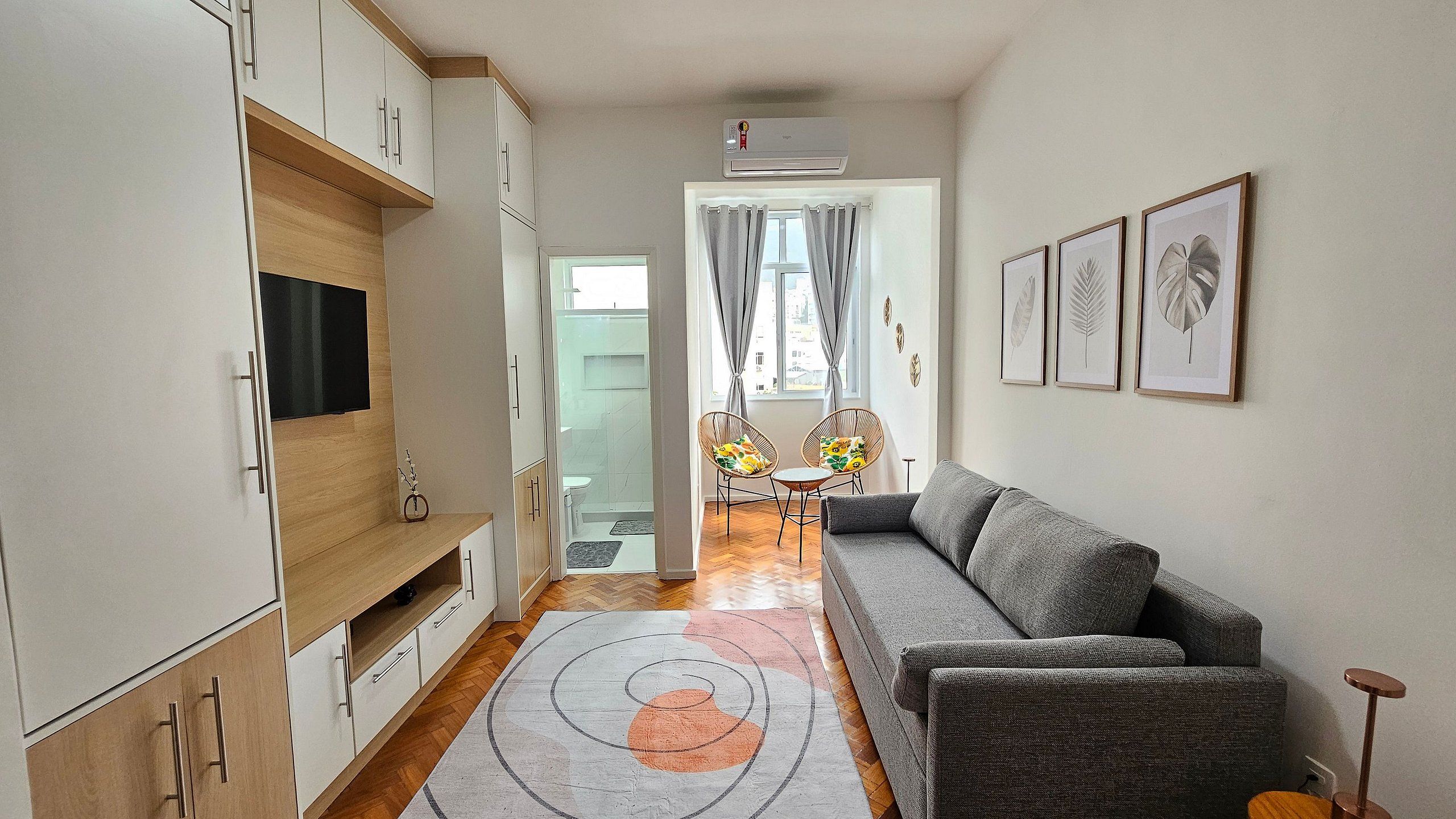 A modern living room with a grey sofa, wooden cabinets, a flat-screen TV, and a patterned rug.