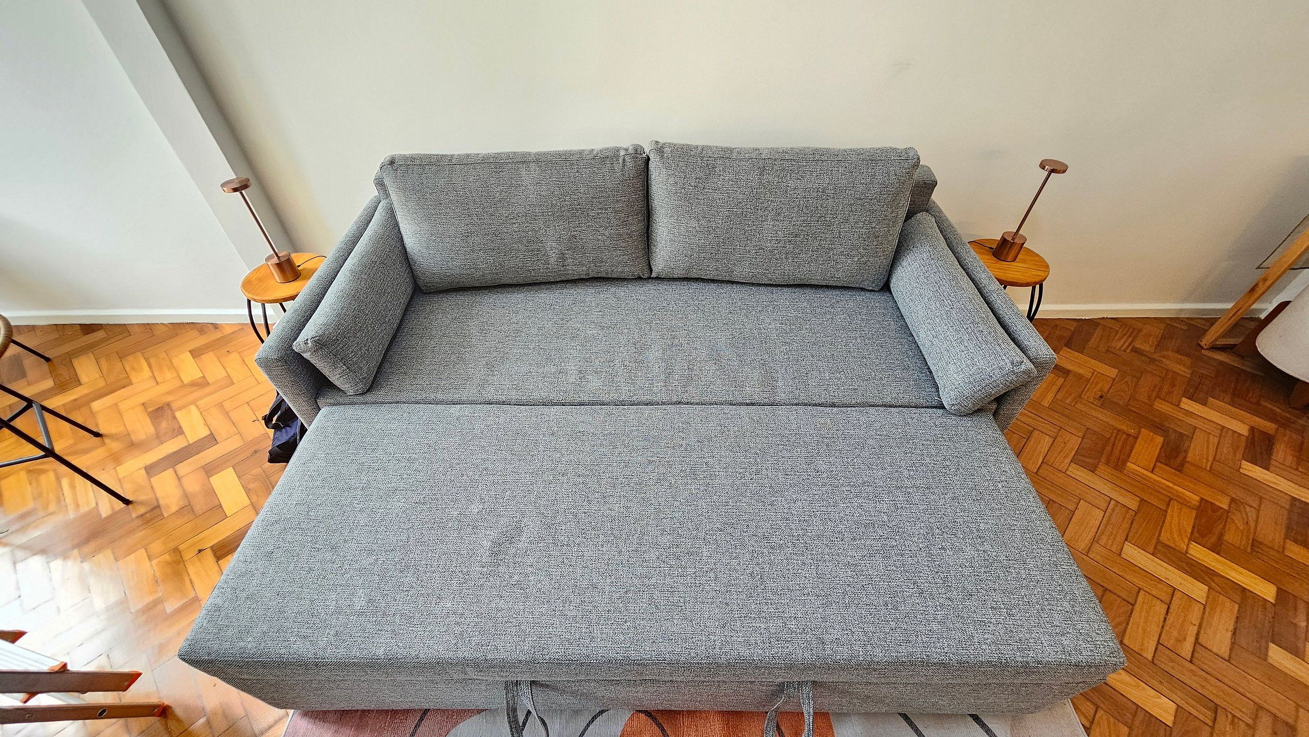 A grey sofa in a room with wooden parquet flooring and two small round tables with copper-colored legs.