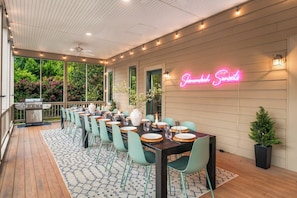 Un espace de restauration en plein air agrémenté d’un panneau lumineux au néon, d’une terrasse en bois et offrant une vue sur un jardin.