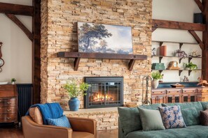 A living room with a stone fireplace, a painting above it, and a sofa with cushions.