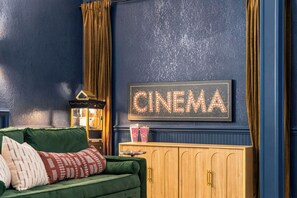 A cozy room with a green sofa, a wooden cabinet, and a wall-mounted sign that reads 'CINEMA'. - Shenandoah Luxury: Views and Privacy w/ Hot Tub, Sauna, Theater (Stanardsville)