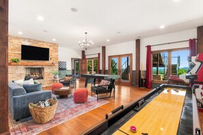 A spacious living area with a fireplace, comfortable seating, a pool table, and a shuffleboard table.