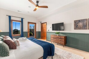 A bedroom with a bed, a dresser, a television, and a view of a staircase and outdoor scenery.