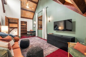 A cozy living room with a television, a desk, a chair, and a bookshelf.