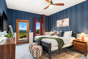 A bedroom with a bed, bedside table, lamp, and a view of the outdoors.