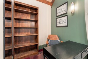 A room with a wooden bookshelf, a desk, and two framed artworks on the wall.
