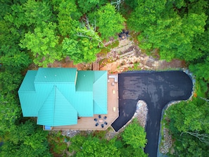 Een luchtbeeld van een huis met een groen dak, een terras met buitenmeubilair en een oprit die leidt naar een zwart waterlichaam.