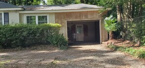 Une maison avec la porte du garage ouverte, entourée de verdure et donnant sur une allée gravillonnée.