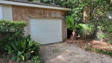 A garage with a white door, surrounded by greenery and a gravel driveway.