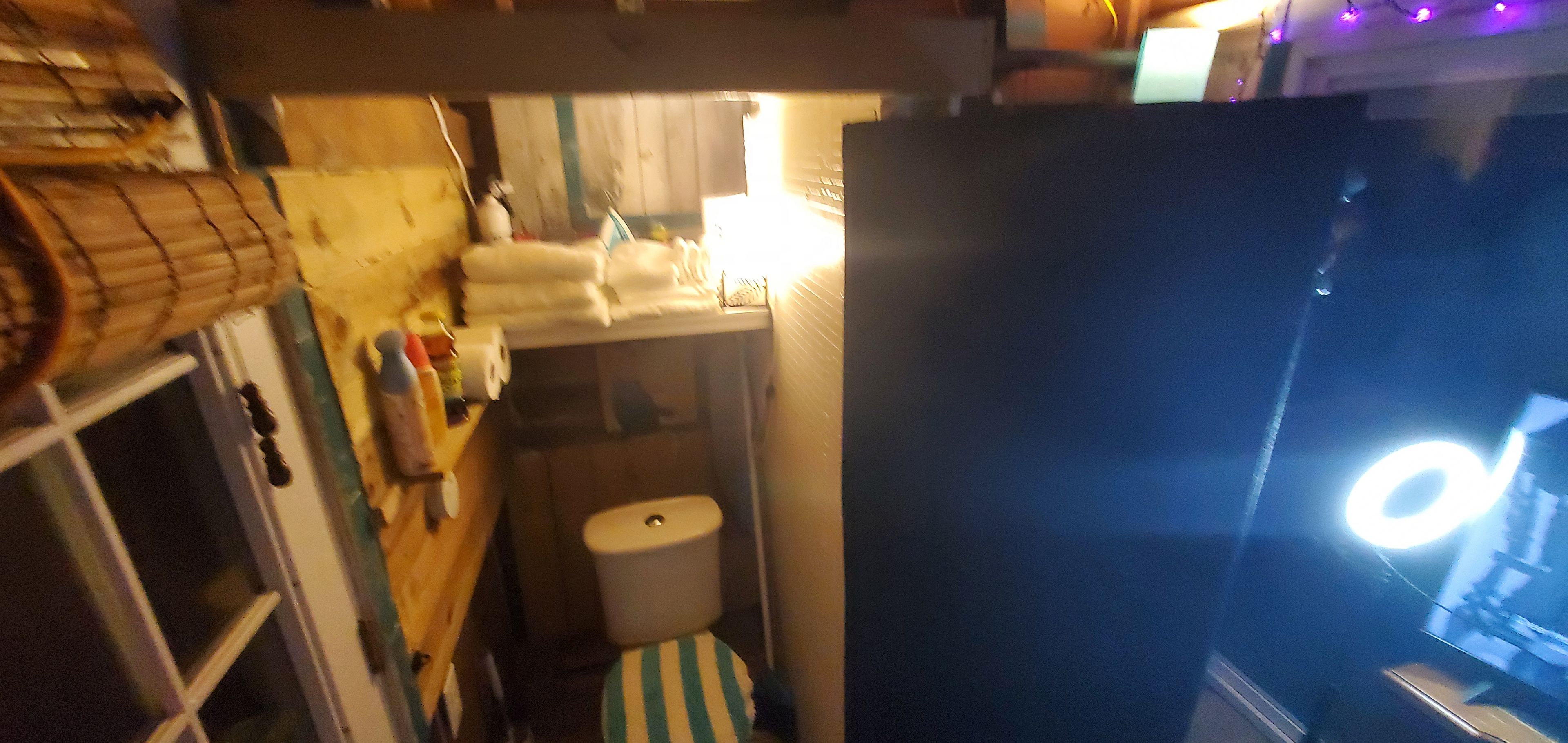 Ett litet badrum med en toalett, en liten hylla med toalettartiklar och en randig badrumsmatta.