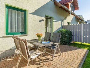 A patio with a table and chairs, a small garden, and a house with a red roof. - Holiday Apartment With 1 Bedroom (Heringsdorf)