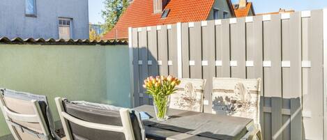 An outdoor patio with a table and chairs, a vase with flowers, and a wooden fence.