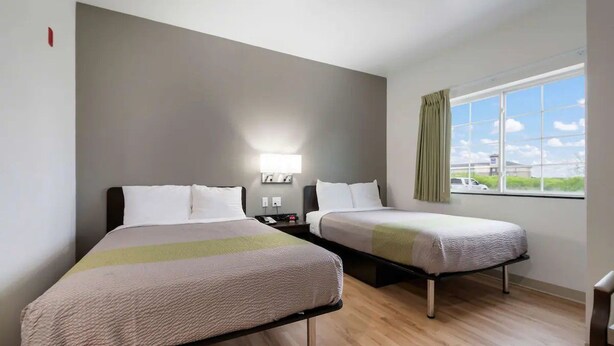 Ett hotellrum med två sängar, ett nattduksbord, en lampa och ett fönster med utsikt.