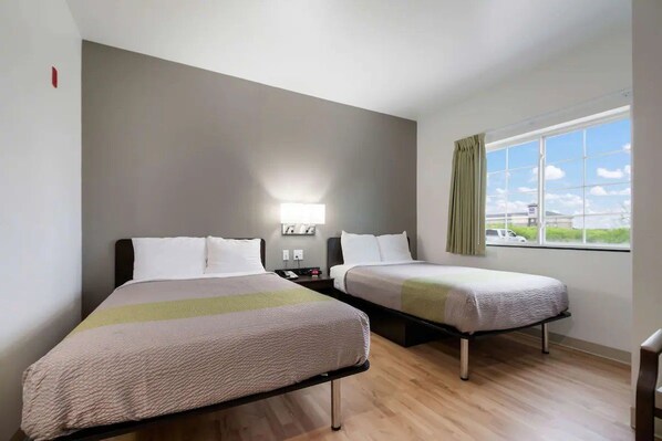 Ein Hotelzimmer mit zwei Betten, einem Nachttisch, einer Lampe und einem Fenster mit Blick.