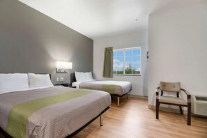 Ein Hotelzimmer mit zwei Betten, einem Sessel, einem Fenster mit Vorhängen und einer Wandlampe.
